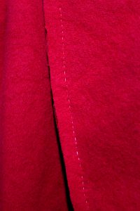 Running stitched seam in linen thread on red wool